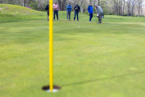 Closeup of golf hole with flag, men playing golf in background